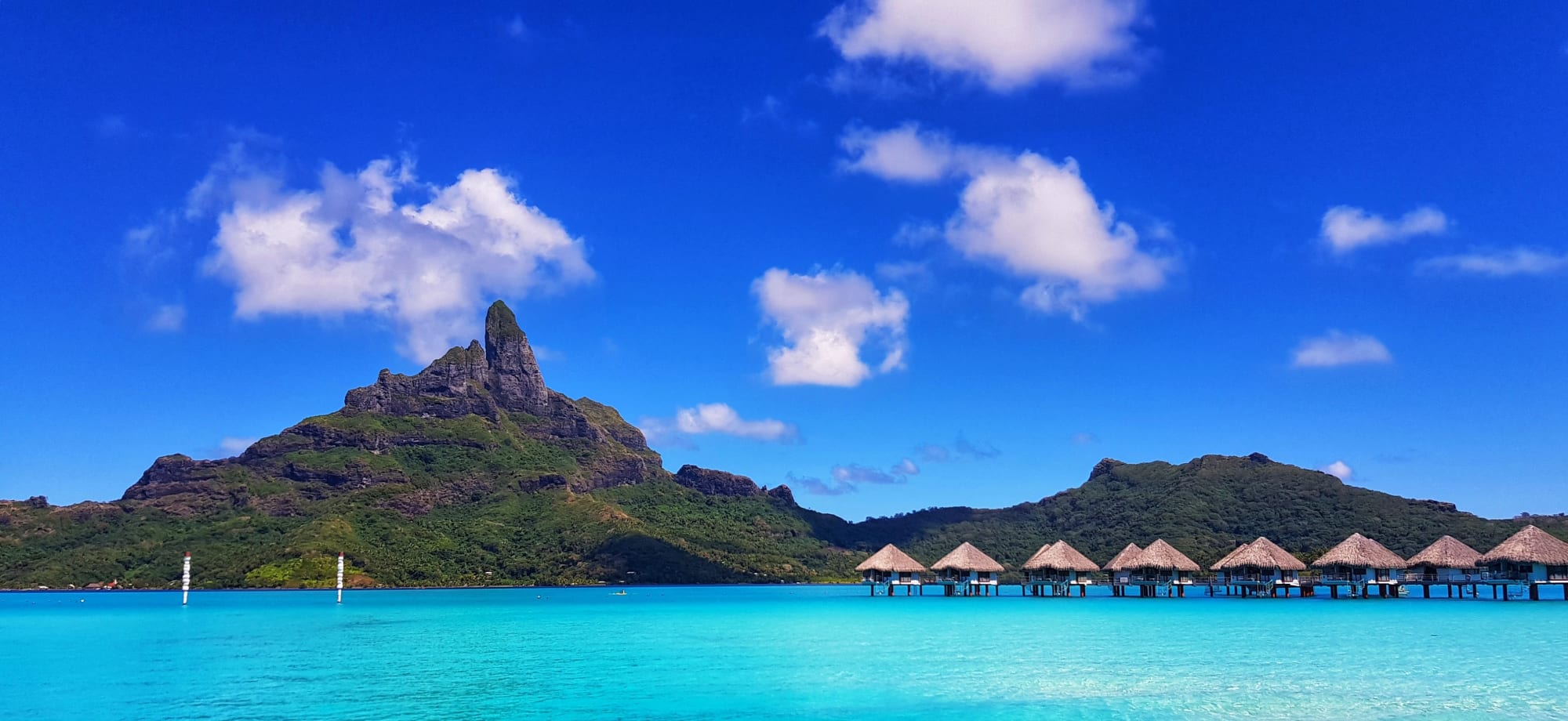 Overwater villas are sitting in the turquoise ocean, backed by massive mountains.